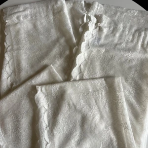 Vita spetsgardiner med volangkant - Superfina vita gardiner i spets med blommigt mönster och dekorativ volangkant längs sidorna. Tunt och luftigt material. 2 st