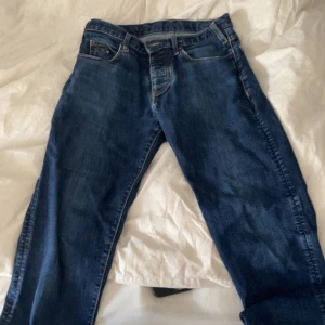 Blå jeans från Emporio Armani - Snygga blå jeans från Emporio Armani med klassisk femficksdesign och ikonisk logga på bakfickan. Jeansen har orange kontrastsömmar och är tillverkade i mjukt denimtyg som sitter skönt. Perfekta för dig som gillar stilrena och tidlösa jeans.