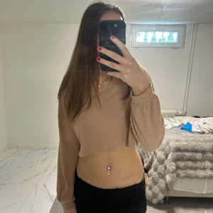 Beige croppad ribbad långärmad topp - Säljer en beige croppad topp med ribbad struktur och v-ringad hals. Toppen har långa ärmar med lätt puff och är tillverkad i ett mjukt stickat material. Perfekt för dig som gillar en chill och trendig look. Passar även dig som har storlek S