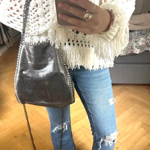 Silver axelväska med kedja - Snygg axelväska i glittrigt silver med kedja som axelrem och coola detaljer längs kanterna. Väskan har en mjuk form och passar perfekt för att lyfta din outfit med lite extra shine. Perfekt storlek för mobil, plånbok och småsaker.påminner om Stella mccartney väskan💓💓
