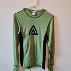 Grön långärmad tröja från Aclima strl XS - Stort svart logotryck på bröstet och tumhål vid mudden. Tröjan har en stor ficka på magområdet. Orginal hade tröjan en luvan men har klippts bort och har sytts och designats för hand. Aldrig använd. Tillverkad i 100% merinoull. 