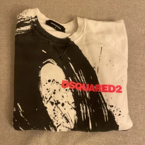 Vit och svart sweatshirt från Dsquared2 - Säljer en vit sweatshirt från Dsquared2 med svart grafiskt tryck och röd logga framtill. Tröjan har rund halsringning och långa ärmar. Materialet är mjuk bomull, perfekt för dig som gillar streetstyle och statement-plagg.