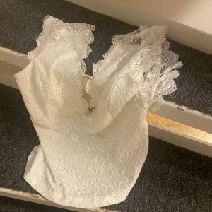 Vit spetsblus med volangdetaljer - Säljer en vit blus i spets med v-ringad hals och breda volangprydda axelpartier. Blusen är perfekt till fest och nästintill oanvänd