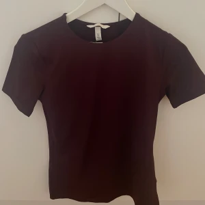 Mörk vinröd topp från H&M med prislapp kvar  - Snygg vinröd topp från H&M i storlek S. Modellen är enkel med rund halsringning och korta ärmar. Materialet är mjukt och stretchigt, perfekt för en clean och stilren look. Passformen är slim och toppen är enfärgad utan detaljer. Prislapp sitter kvar orginalpris 150