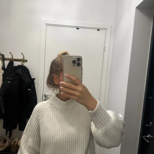 Vit ribbstickad polotröja - Supermysig vit ribbstickad polotröja med breda ärmar och hög krage. Tröjan har en loose fit och är perfekt för kyliga dagar. Materialet känns mjukt och värmande, och den ribbade strukturen ger en snygg och trendig look.