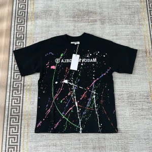 Svart t-shirt med färgstänk från Maison Margiela - Cool svart t-shirt från Maison Margiela med färgstänk i grönt, rosa, vitt och lila. Tryckt logga framtill och klassisk rund hals. Perfekt för dig som gillar streetwear och vill sticka ut. Ingen pris lapp kvar med helt ny nästan 