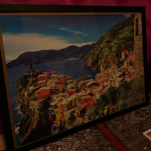 Inramat pussel med havsmotiv - Ett pussel med motiv av en kuststad och är inramad. 