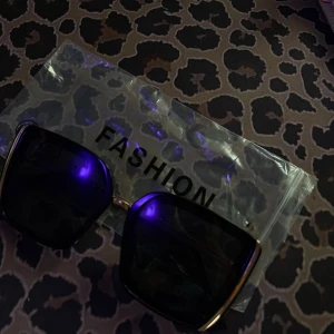 Svarta fyrkantiga solglasögon - Snygga svarta solglasögon med stora fyrkantiga bågar och tunna guldfärgade detaljer. Perfekta för att ge en cool vibe till din outfit. Kommer med ett plastfodral märkt 'FASHION'.