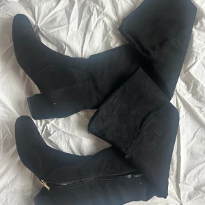 Svarta mockastövlar med klack - Säljer ett par svarta stövlar i mocka med låg klack och spetsig tå. Stövlarna har dragkedja på insidan för enkel på- och avtagning. De är höga och har en stilren, klassisk look som passar till många outfits. Dom är uppsprättade där uppe som du kan se på sista bilden❣️ säljer om efter att dessa inte passade mig, skicka privat för mer mått och bilder!🤞🏻❣️