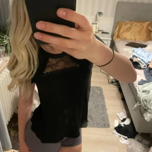 Svart blus med spets från H&M - Svart blus från H&M med korta ärmar och snygga spetsdetaljer över bröstet. Rund halsringning och mjukt material som sitter skönt. 