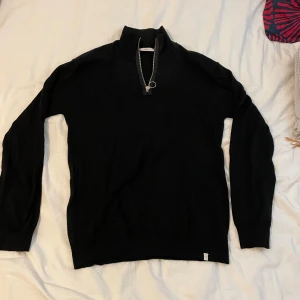 Svart stickad half zip från Minimum - Svart stickad tröja från Minimum med half zip och hög krage. Tröjan har långärmade ärmar. Tröjan är gjord av premiumull och är av mycket hög kvalitet.