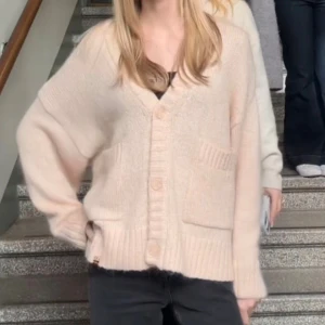 Rosa/aprikos trendig cardigan  - Mysig rosa/aprikos stickad kofta med v-ringning och stora knappar framtill. Koftan har två framfickor och ribbade muddar vid ärmslut och nederkant. Passformen är loose och ärmarna är långa, perfekt för lager på lager under kyliga dagar. Storlek M/L💗
