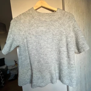 Grå stickad tröja från Pieces - Mysig grå stickad tröja från Pieces i storlek XS. Tröjan har korta ärmar och en ribbad rund halsringning. Perfekt för lager-på-lager och chill dagar. Den har en loose passform och är tillverkad i ett mjukt stickat material. Ärmarna är avklippta själv men märks inte!