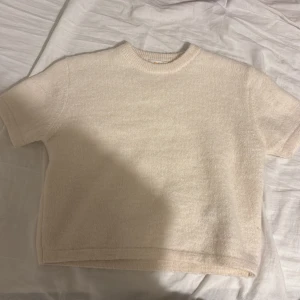 Stickad kortärmad topp - Mysig beige stickad topp med korta ärmar och rund hals. Enkel och stilren design som är lätt att matcha med olika outfits. Perfekt för dig som gillar en clean och chill look. Materialet är mjukt och ger en skön känsla mot huden. Toppen är från GinaTricot.