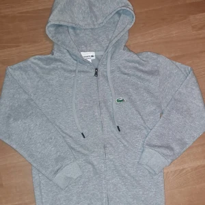 Lacoste zip-up - Grå snygg lacoste zip up hoodie i nyskick, använd ca 3-4ggr. Står S men är mer XS.                                                      Priset är ej hugget i sten.