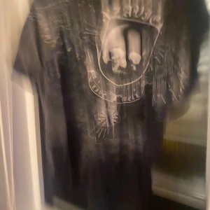 Affliction  - Cool svart t-shirt med stort döskalletryck och vingar på bröstet. T-shirten har korta ärmar och en avslappnad passform. Perfekt för dig som gillar rockig stil och vill sticka ut med ett unikt motiv.