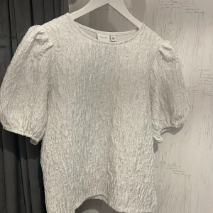 Vit puffärmad topp från Vila - Säljer en vit topp från Vila med puffiga korta ärmar och snyggt skrynklat tyg. Toppen är endast använd 1gång!.