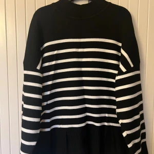 Svartvit randig stickadtröja  - Svart och vit stickad polotröja med ränder och lång ärm. Tröjan har en hög krage och slits på sidorna. Stickad i mjukt material som känns skönt mot huden. Perfekt för dig som gillar en chill och stilren look.