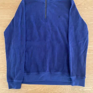 Blå half zip tröja från Polo Ralph Lauren - Mörkblå långärmad tröja från Polo Ralph Lauren med broderad logga på bröstet. Tröjan har half zip-dragkedja vid halsen och är tillverkad i mjuk bomull. Perfekt för lager-på-lager och chill stil.