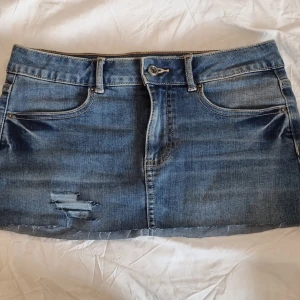 Blå jeanskjol i minilängd xs/s - Storleken är s men passar mig som har xs Säljer en klassisk blå jeanskjol i minilängd med slitna detaljer framtill. Kjolen har knapp och dragkedja framtill samt rå kant nertill. Perfekt för en avslappnad och trendig look.