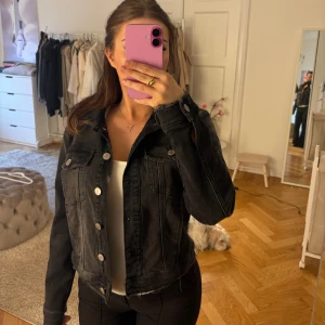 Svart jeansjacka från Zara - Svart jeansjacka från Zara med silvriga knappar och rå, fransad nederkant. Klassisk modell med två bröstfickor och krage. Jackan har en lite tvättad look och raka, långa ärmar.