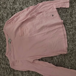 Ljusrosa långärmad tröja Hampton Republic - Supersöt ljusrosa långärmad tröja från Hampton Republic med liten spetsdetalj på bröstfickan. Tröjan är i mjuk bomull och har en klassisk passform. Perfekt för dig som gillar en enkel men gullig stil.