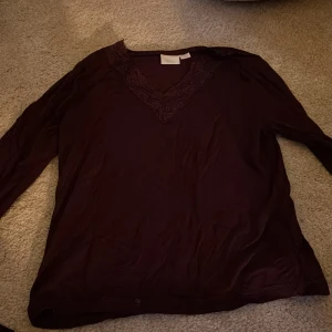 Mörklila blus med spets från Gina Tricot - Säljer en mörklila blus från Gina Tricot med lång ärm och snygg v-ringning dekorerad med spetsdetaljer. Blusen har en mjuk och följsam känsla, perfekt för dig som gillar stilrena plagg med en twist. Passar dig som vill ha något lite extra i garderoben.