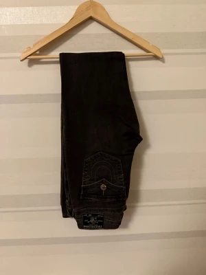 True Religion Becca Bootcut Jeans Svart - Svarta jeans från True Religion, modell Becca Mid Rise Bootcut. Snygga kontrastsömmar och ikoniska ficklock med silverfärgade knappar. Klassisk bootcut-passform och midwaist. Perfekt för dig som gillar street och premium denim.