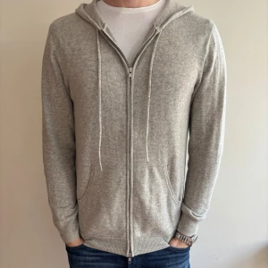 Kashmir hoodie - Snygg ljusgrå kashmirhoodie med huva och snörning, hel dragkedja framtill och två fickor. Tröjan är stickad i kashmir. Perfekt för chill dagar och enkel att matcha med jeans. Köpt från John Henric, använd sparsamt helt utan defekter.