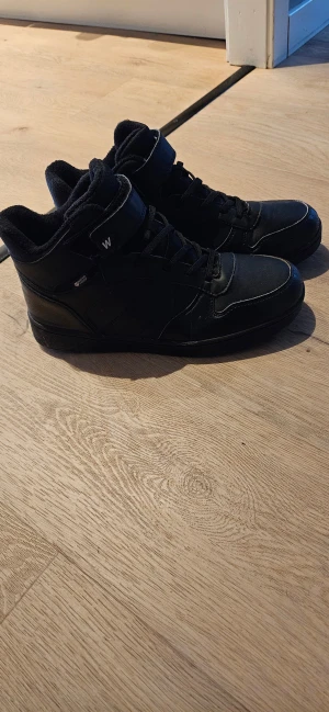 Svarta water propf sneakers med foder, snörning och kardborre - Svarta sneakers från Walkers med snörning och kardborreband upptill. Skorna har robust mönstrad sula för extra grepp och är tillverkade i syntetmaterial med detaljer i skinnimitation. Perfekta för dig som gillar en sportig och clean look.Water proof och fodrade.