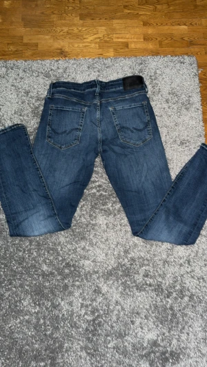 Jack&jones blå jeans W31 L32 - Snygga blå Jack&jones jeans. Jeansen har en mörkblå tvätt med lätt slitning och detaljer i kopparfärg. Perfekt passform med normal midja och smalare ben, passar till allt.