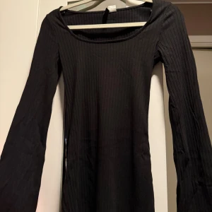 Svart ribbad långärmad klänning - En svart, ribbad klänning med lång ärm och rund halsringning. Modellen är figurnära och har en enkel, stilren look som passar perfekt för dig som gillar minimalistisk stil. Materialet är mjukt och stretchigt för en bekväm passform.