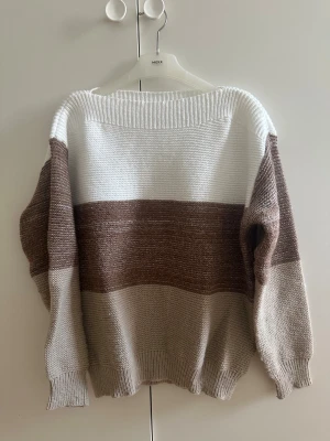 Randig stickad tröja - Säljer en mysig stickad tröja med breda ränder i vitt, brunt och beige. Tröjan har långärmad design, ribbad hals och muddar. Perfekt för dig som gillar chill och stilrena färger. Passar till jeans eller mjukisbyxor