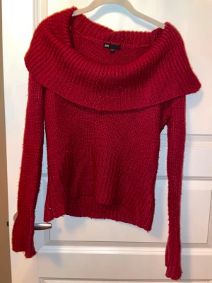 Röd stickad offshoulder-tröja JSFN - Snygg röd stickad tröja från JSFN med bred offshoulder-krage och långa ärmar. Tröjan har ribbade detaljer vid krage, ärmslut och nederkant. Perfekt för dig som gillar en chill och trendig look med lite extra attityd.