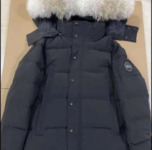 Canada Goose jacka - Säljer en svart dunjacka från Canada Goose med stor fluffig pälskrage och klassisk logga på ärmen. Jackan är lång, har knappar och dragkedja framtill samt flera fickor. Perfekt för kalla vinterdagar och riktigt snygg streetstil.