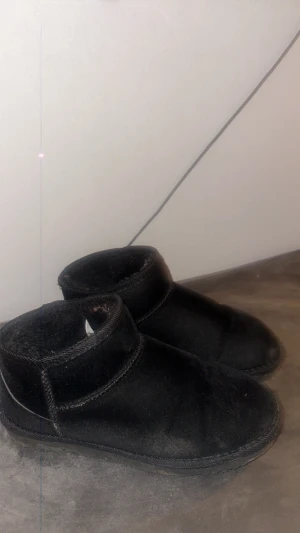 Svarta boots i mocka - Mysiga svarta boots med låg skaft och rund tå. Utsidan är i mjuk mocka och insidan är fodrad för extra komfort. Perfekta för kalla dagar och har en platt sula som gör dem sköna att gå i. Enkel och stilren design som passar till det mesta.lager157