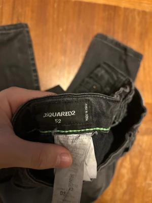 Svarta skinny jeans från Dsquared2 - Svarta jeans från Dsquared2 i storlek 52 med skinny passform. Jeansen har slitna detaljer, hål och en tvättad look. Klassisk femficksmodell med Dsquared2-logga vid gylfen och grön söm på insidan. Tillverkade i stretchig denim för skön känsla.