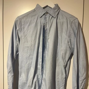 Ljusblå klassisk skjorta från Massimo dutti  - Snygg ljusblå skjorta med klassisk krage och knappar framtill. Skjortan har lång ärm och är tillverkad i mjuk bomull, perfekt för en clean och stilren look. Passar dig som gillar enkel och tidlös stil.