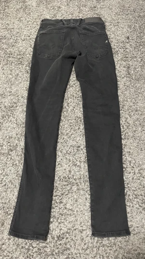 Svarta Replay Anbass jeans, slim fit - Säljer ett par svarta Replay Anbass jeans i storlek 27. Modellen är slim fit med klassisk femficksdesign, svarta sömmar och Replay-logga på bakfickan. Jeansen är tillverkade i stretchigt jeansmaterial för en bekväm passform. Hör av er för frågor📸 