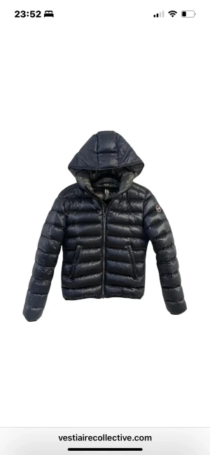 Svart dunjacka från Colmar med huva - Svart, glansig dunjacka från Colmar med huva och dragkedja framtill. Jackan har ett quiltat mönster, två sidofickor med dragkedja och en rund Colmar-logga på ärmen. Perfekt för kalla dagar och har en snygg, normal passform.