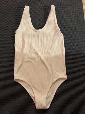 Beige ribbad body från Zara - Säljer en snygg vit body från Zara i storlek M-L(liten i storleken XS-S). Modellen är enkel med breda axelband och rundad halsringning. Materialet är ribbat och känns mjukt mot huden, perfekt för strandhäng eller poolen. Stilren och lätt att matcha med en sarong eller shorts.