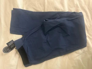 Mörkblå kostymbyxor från Peak Performance - Snygga mörkblå golfbyxor  från Peak Performance med rak passform och klassisk design. Byxorna har diskreta fickor och en stilren midja med svarta detaljer på insidan. Perfekta för dig som gillar en clean och modern look.