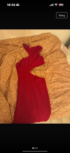 Röd asymmetrisk klänning med cut-out - Säljer en röd, tight och ärmlös klänning med asymmetrisk design och cut-out vid midjan. Klänningen har en slits på sidan och är i ett stretchigt, strukturerat tyg. Perfekt för dig som vill sticka ut med en trendig look.