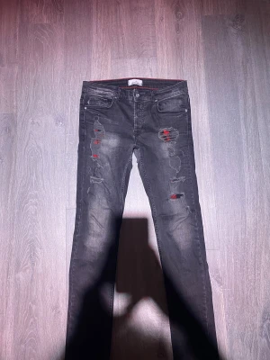 Svarta skinny jeans från Stone Island - Säljer ett par svarta skinny jeans från Stone Island med detaljer och röda inslag under de partierna. Jeansen har fem fickor, knappgylf och en snygg tvättad look. Perfekt för dig som gillar streetstyle och vill sticka ut. Saknar bara stone island badges