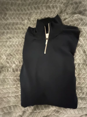 Svart half zip tröja Lindbergh - Svart långärmad tröja från Lindbergh med slim fit-passning och half zip-dragkedja framtill. Hög krage och stilren design, perfekt för dig som gillar minimalistiskt och cleant. Materialet känns mjukt och skönt mot huden.