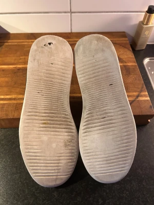 Svarta mockasneakers från Sandays - Svarta sneakers från Sandays med ovandel i mocka och detaljer i svart skinn vid hälen. Skorna har snörning med metallöglor och en vit platt sula. Snygg och stilren design med rund tå och diskret logga i guld på plösen. Litet hål under skon men går inte in i skon. Nypris 2199:-