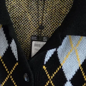 Rutig kofta från Vero Moda - Snygg kofta från Vero Moda med rutigt mönster i svart, vitt och gult. Koftan har knappar framtill och en klassisk krage. Stickad i mjukt material som passar perfekt för kyliga dagar. Perfekt för dig som gillar retrovibbar och vill sticka ut. Upplever den som mera M i storlek. Nypris 449kr