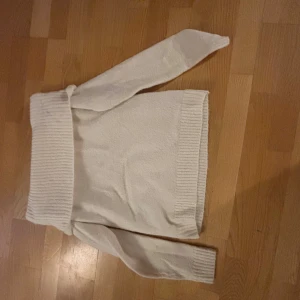 Vit stickad polotröja med ribbad kant - Säljer en vit stickad polotröja med bred, ribbad krage och ribbade muddar vid ärmslut och nederkant. Tröjan har lång ärm och är perfekt för dig som gillar en enkel och clean look. Passar dig som vill ha en mysig och stilren tröja till garderoben.