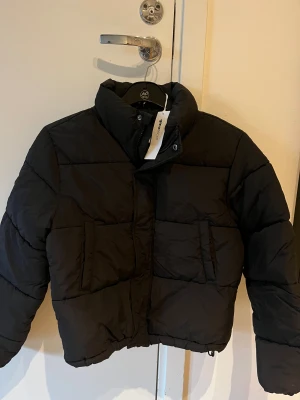 Svart pufferjacka från Gina Tricot,flickjacka 146/152 - Snygg svart pufferjacka från Gina Tricot med hög krage och stora fickor framtill. Jackan har en boxig, lite croppad passform och stängs med dragkedja och tryckknappar. Stl 146/152