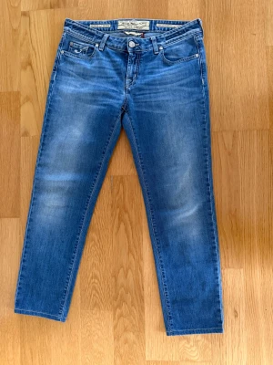 Jacob Cohen blå jeans - Snygga blå jeans från Jacob Cohen. Jeansen har ljusa slitningar framtill och bak, kontrastsömmar och en broderad J på myntfickan. Tillverkade av japanskt tyg med italienskt hantverk. Perfekt för dig som gillar stilrena jeans.